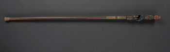 (UEM19280)&amp;#160;A wooden sceptre and ceremonial staff of authority, where the upper part is carved in the form of a human-like female figure with her knees bent, as if seated. The figure is adorned with a prominent headdress, green necklaces, and brass or copper anklet rings, and is dressed in a blue loincloth only. The staff signifies leadership and social rank. Sophistically carved wooden artefacts decorated with metal elements were used in rituals and ceremonies. Symbolically, the ceremonial staff represents royalty, local traditions and beings within the spiritual realm. Material: Wood, brass, copper, glass, and cotton Region: Haut Kasai, Lunda Length: 94 cm. Arrival: Donated to the Museum by Lieutenant Finn Hannibal Kjelstrup, 1911.