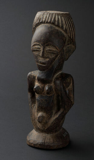 (UEM26978)&amp;#160;Wooden Power Figure/ Nkisi carved in the form of a double female figure resting on a pedestal with no legs. The figure(s) show a distended abdomen and pendant breasts, symbolising fertility. Nkisi is a spiritual object that embodies healing and sacred components. The two figures together represent female aspects of spirituality. It contains spiritual substances, often concealed within the figure, used for protection, fertility, and the well-being of the community. Material: Wood Region: Kasai Oriental, Songye Height: 30 cm. Arrival: Donated to the Museum by Dr Inge Heiberg, 1926.