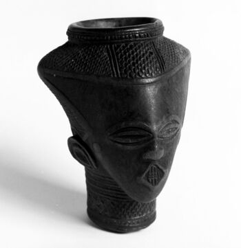 (UEM7615)&amp;#160;A palm wine drinking vessel carved in human-like shape, portraying the head of a man or perhaps, a woman. Among the Kuba, most vessels made for palm wine drinking were sculpted in the shape of male figures. Ideally, palm wine drinking was a social activity for men, not women. This does not mean that women could not also enjoy palm wine, only that if they did so, they would not drink it in the company of men. Compared to the previous presented drinking vessels, this one is less elaborate, although the face, hairstyle, and necklace or tattoo are carefully carved. Material: Wood Region: Kasai, Kuba Height: 20 cm. Arrival: Bought by the Museum from Christian Martini and Christian Schønberg, 1890.