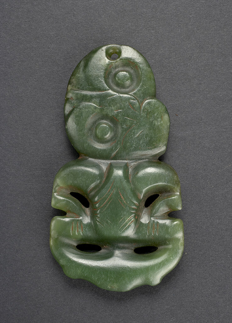 (UEM144a) Pendant or hei tiki. 9,4 cm. The hei tiki is a very stylised representation of the human form. Usually considered either female or genderless. The splayed hips, sometimes dilated vulva, bulging eyes and hands akimbo is considered to be representations of a woman in childbirth and thus the object can also be associated with gods of fertility. Made from jade (nephritt), these antropomorphic pendants are considered one of the most valuable taonga (treasured possesion) amongst the Māori. Jade is commonly found on the South Island of Aotearoa, New Zealand, yet the hei tiki is usually associated with the North Island. Due to the valuable nature of the hei tiki, the object is usually connected with the upper class amongst Māori, giving the object mana (power). Though not precisley dated, the hei tiki can be traced back to the Classical Māori period (Te Puawiatanga, 1500-1800).    The object was collected by Fredrik Ring in Valparaiso, Chile in the 1820s. Konsul Ring donated the object to the Ethnographic Museum in 1833. Material: Jade/semiprecious stone Region and culture: Hokianga, New Zealand - Maori