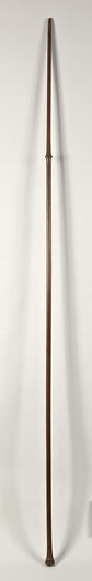 (UEM185) Wooden lance or staff. Though its documentation states it derives from New Zealand, most likely it originated in the Austral Islands, due to its conical knot being identical to the wooden paddle (UEM160). The staff is approximate 2,3 m long. The knot consist of eight carved human heads, followed by a field of carved zig-zagging shark tooth patterns, along with a linear pattern field as well. The entire staff is very finely polished. The object had most likely a ceremonial function. Its production date is not known, but it was probably acquired around 1856. The lanse would have been carved with either metal tools introduced after European contact or with their own indigenous carving tools such as shark teeth or shell. Most objects from the Austral Islands are composed of three design elements: concentric circles, minute rows of nested crescents, and x-shaped motifs. However, the motifs found on different objects are used in such a vast array of combinations, that no two objects would appear the same. Material: Wood Region and culture: Possible Cook Island, French Polynesia or New Zealand