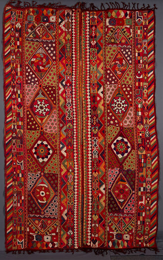 UEM49198. Triple borders at each vertical edge of the two panels. Outer edge of each panel has the characteristic multi coloured diagonal lines pattern. The other borders have geometrical /vegetal motifs. In the centre length wise are four big diamonds surrounded by a pattern of uniform flowers. All four ends of the panels are closed in with a triangle in which a human fig. Other motifs elsewhere: birds, flowers and trees.