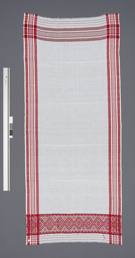 (UEM46987) Gamusa has become a kind of identity symbol for Assamese society. Young girls first learn to weave different patterns in gamusas . Gamusa is a part of all rituals. Men and boys wear gamusas as headgear and around the waist, especially during Bihu (the spring festival). Gamusas are given as gifts to respected guests. In weddings, relatives and respected guests receive gamusas from the bride, preferably woven by her. Material: Cotton. Guwahati, Assam district.