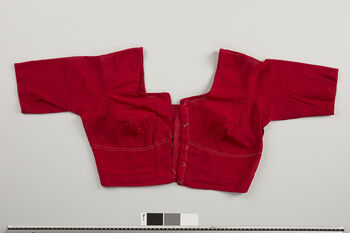 (UEM46996) This is a common sari blouse worn throughout India. In Assam, it is now worn with almost all local cultural women’s clothing. In the Karbi community, older women are still seen wearing pekok , etc., without a blouse underneath, or possibly Jir-ik (see UEM46900 and UEM46901 ). Before the blouse arrived, women in Assamese society used a long piece of cloth called riha , which was wrapped around the chest. Today, riha is used for special ritual occasions and by the bride at weddings, often now worn over a sari blouse. As the blouse is a relatively new manufactured garment it has not got local names and is called just blouse even if it is stitched of local woven fabric. Material: Cotton. Assam district.