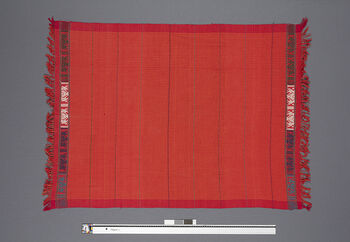 ( UEM 46856) Loin loom, plain weave, pick-up pattern on the weft. Name of pattern edging: half fan pattern. Everyday use. Worn on upper body. Folded in two, two fringed ends in a corner are tied together. The garment is worn so that this fringed knot hangs over the left shoulder, while the loop hangs under the right arm. Currently, people usually wear a sari blouse underneath but didn’t in the past. Elderly people in the villages do not wear garments underneath. Worn over pini see UEM46842 – UEM46848. Woven by Basapi Engtipi. Rongchingdon, West Karbi Anglong.