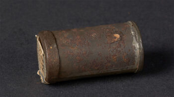 (UEM13946) Description: "A small, rounded piece of bone (or similar) referred to as the Burmese charm" (Catalog text). Classification: Magic / Preventive medicine. Material: Tin (metal). Dimensions: Length: 4.4 cm. Collection history: Gift of Mr. and Mrs. Hunt. Collected by Dr. J. Reid. "An original certificate from the official who first delivered it to the museum in Travancore is included, from where it was disposed of in 1904" (Translation from the original Norwegian catalog card).
