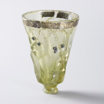 Drinking glasses were not commonplace in the Iron Age, so those who were fortunate enough to own such valuables took good care of them. There was no glass production in Scandinavia, so the glasses came from far away; from the Black Sea region, the Continent and eventually also from England. Should the worst happen anyway – that someone dropped a glass on the floor and it broke, it was carefully repaired. This glass goblet is repaired with decorated and gold-plated silver fittings. Such repairs were difficult and required expertise. A specialized craft centre for glass repairs probably existed in the southwest of Norway. The glass may already have been 100 years old when it was repaired sometime in the first half of the 6th century AD. Repaired glass cup from Snartemo in Vest-Agder. C26001.