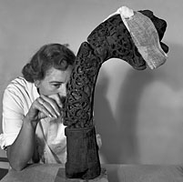A black and white photo showing a woming examining the wooden carved snake.