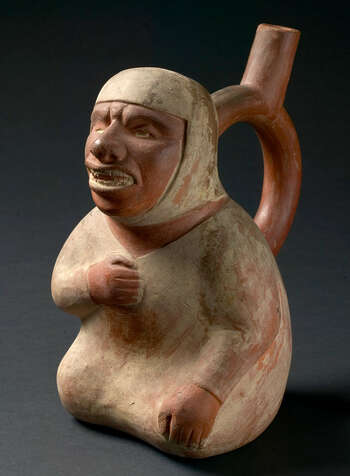 (UEM9967) Bottle in form of a seated blind man dressed in a simple white tunic and head dress, one hand on his chest. Mold made. Polychrome painting: white on brown. Moche, 100–800, Peru.