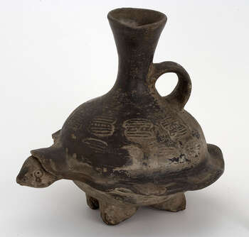 (UEM9969) The vessel depicts a turtle on four feet with a funnel shaped vertical spout and a handle. Opposite to the handle the turtle´s head is modelled. On the turtle’s shell 8-shaped signs are engraved. Mold made. Smudge fired black ware. Colonial?Chimú-Inca tradition. Around 1550?, Peru.