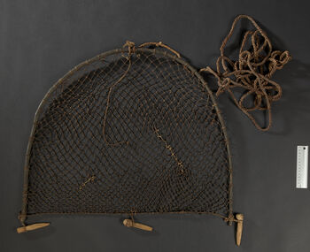 (UEM12193)&amp;#160;Rev. Bodding’s notes: 'The procedure for using this trap is the following: At places where these birds are seen to bath in sand, grain or other foods are distributed to habituate them to come there. The trap is set by hammering the attached sticks into the ground while the net is held down with the help of a thin twig. Just in front, at a distance equaling the hight of the trap, a wooden hook is knocked into the ground, and the long rope is led under the hook. The trapper sits at a distance, behind a bush, with the end of the rope. When a sufficient number of birds have gathered, he pulls down the trap. The inserted sticks hold the net down so the birds cannot escape.' Material: Wood, vegetable fibre.&amp;#160;Height: 58 cm, width: 70 cm.