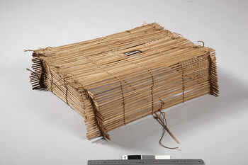 (UEM12214) Rev. Bodding’s notes: 'Especially used in fields where the birds have become used to come to feed.As bait is spread the same kind of seed that grows there. A stone is placed on the top hole, partly to prevent birds from escaping, partly to hold the trap down by its weight. Through this hole the bird is taken out. Normally the hands of the Santals are not bigger than that this can be easily done. The same mechanism as the one in this trap is also used for catching rats. Then just a stone slab or a strip of wood is used instead of the bamboo wicker.' Material: Vegetable fibre, bamboo. Length: 56 cm, width: 47 cm, height: 16 cm.