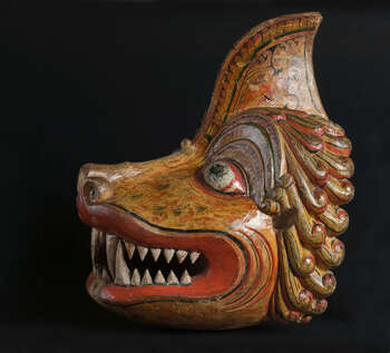 Ritual Function and Context: Kōlam theatre. UEM7007 represents a character of Lion. The mask is known as Simhāyā. The character appears with two or more masks of lions and narrates Simhā-Kōlam in Kōlam Theatre. The key iconographic features of UEM7007 are: • Stylization of natural features of Lion. • Lion’s hair ( kēsarā/sadāpalū ) carved in the pattern of Sinhālese motifs ( mōstarā:  liyāweĺ ) • The widely opened mouth and sharpen tooth and tusks remind the masks of Rākshā cult. • Yellow is the dominant colour. • Deep and widely opening mouth provides access to the dancer wearing this mask to look through the audience. • Influence of the iconographic features of Buddhist art in temples. • Ears attached separately (these features are missing in this mask) Tradition: Southern Dance Tradition/Low-Country Dance Tradition. This tradition is popular in Mātara, Bentōta, Ambalaňgoda in the Southern province and Olabodūwa in Rāiygama Kōralē in Western province of Sri Lanka. Materials and Techniques: Polychrome carved wood (white, yellow, red, blue, green, black).