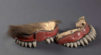 Ritual Function and Context: Sanniyäkuma / Dāha-atā sanniya/paliya. UEM 7013 (2) is the mouth of a character from Pali Masks. This fragmented mask ( kata-muhunu ) is one of the twelve (arguably sixteen or eighteen) characters that appear in an intermediate time in Sanniyäkuma ritual. This character brings two fire torches ( pandām ) and increases flames by throwing local flammable herbal powder called Dūmmāla taken from a special tree grown in Sri Lanka. The choreography of this character is extremely dynamic and aggressive. The masked play in this ritual is full of conversation, humor, and interaction with both drummers and the sick person ( ařthūrayā ) to whom the ritual is held for. The key iconographic features of UEM7013 (2) are: • Pieces from larger size masks from Sanniyäkuma ritual. • Mask comes in fragmented pieces ( katā-muhunū ) as nose, eye balls or upper and lower lips. • Large white face (pale white or yellow) with widely opened and movable mouth with two tusks. • Lion/pig shaped ears, which are missing in this piece. • Mask is completed with heavily grown hair like lion Tradition: Sanniyäkuma or Dāha-atā sanniya / the Southern Dance Tradition/Low-Country Dance Tradition. This healing ritual is believed to be originated from Bali ritual and is popular in Mātara, Gāll, Bentōta, in Southern province and Olabodūwa in Rāiygama Kōralē in Western province in Sri Lanka. Significant difference can be seen in this ritual held according to Mātara Tradition and Bentōta Tradition. Materials and Techniques: Polychrome carved wood (white, yellow, red, black), horse or animal fur, hide, nail, etc.