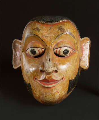 Ritual Function and Context: Kōlam theatre. UEM7021 represents a character village headman. The mask is called Arāchchî. The mask appears in Kōlam Theatre. This mask performs with his assistants’ characters called Henchappū or App. Together, they bring humor to the audience through their conversations. The key iconographic features of UEM7021 are: • Fair/mid skin tone. • Balanced and sharp and refined facial features: eyes, mouth with a slight smile. • Sideburns • UEM7021 is one of the best examples to show the relationship of the iconography of this mask to the Buddhist art in temples. Tradition: Southern Dance Tradition/Low-Country Dance Tradition. This tradition is popular in Mātara, Bentōta, Ambalaňgoda in the Southern province and Olabodūwa in Rāiygama Kōralē in Western province of Sri Lanka. Materials and Techniques: Polychrome carved wood (white, yellow, red, black).
