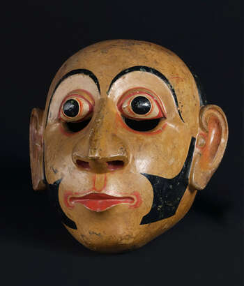 Ritual Function and Context: Kōlam theatre. UEM7023 represents character of higher officials who serve in large areas of a village. This character is known as Mudāli. The mask appears in Kōlam Theatre. Mudāli is present at Kōlam Maduwa with his assistant characters knowns as Appū or LiyanAppū and bring humor to the audience through their inter-reactions. This character represents a higher position in the system of social hierarchy established during this period. The key iconographic features of UEM7023 are: • Fare skin tone. • Carved clear balanced circular face ( vata-kuru-muhūnā )with sharp and refined features of eyes, and the mouth with a slight smile. • sideburn and elongated ears • UEM7023 is one of the refined examples of the mask of Mudāli that shows the influences of the iconography of Buddhist art in temples. Tradition: Southern Dance Tradition/Low-Country Dance Tradition. This tradition is popular in Mātara, Bentōta, Ambalaňgoda in the Southern province and Olabodūwa in Rāiygama Kōralē in Western province of Sri Lanka. Materials and Techniques: Polychrome carved wood (white, yellow, red, black).