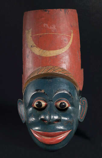 Ritual Function and Context: Kōlam theatre. UEM7033 represents a black foreign character. It narrates a story of the arrival of different ethnic groups to Sinhālese culture. This mask is known as Kaperi-Kōlama. The mask appears in Kōlam Theatre. Kaperi Kōlam performs in Kōlam theatre with groups of other Kaperi masks which include both male and female characters. The key iconographic features of UEM7033 are: • Black or darker skin tone • Wide lips in red colour • Widely opened eyes. • African traditional instrument of Horn or trumpet painted in yellow on the tall red hat is an intricate detail given by mask carver, a clear sign to prove this mask as a black foreign character. That sign could also support to avoid misinterpretation this mask as a Muslim character. • UEM7033 is one of the rare masks in this collection from Sinhālese culture. Tradition: Southern Dance Tradition/Low-Country Dance Tradition. This tradition is popular in Mātara, Bentōta, Ambalaňgoda in the Southern province and Olabodūwa in Rāiygama Kōralē in Western province of Sri Lanka. Materials and Techniques: Polychrome carved wood (white, yellow, red, black, green, blue).