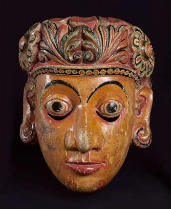 Ritual Function and Context: Kōlam theatre. UEM7036 represents a legendary female character. The mask is known as queen ( bisawā or manāmē bisawā ). The mask appears in Kōlam theatre. In the story related to the character of Manāmē Bisawā, the mask narrates the story of Manāmē Kōlama or a story from the Jâtaka Pothā called Chuĺlā Dhanūďdarā Jātakaya. In Sinhālese rituals and Kōlam dance, all the female characters represent from masks are worn by male dancers. The key iconographic features of UEM7036 are: • Balance pleasing facial form. • The short head-dresses decorated with Sinhala motifs ( môstharā ). • A half-smile ( adavaň sinahawā ) and half circle eyebrows • Fair skin tone • The crown comes in various forms in different regional traditions. A low-height floral headdress is believed to be typical character from Mātara tradition. This is one of the refined examples of this character. Tradition: Southern Dance Tradition/Low-Country Dance Tradition. This tradition is popular in Mātara, Bentōta, Ambalaňgoda in the Southern province and Olabodūwa in Rāiygama Kōralē in Western province of Sri Lanka. Materials and Techniques: Polychrome carved wood (white, yellow, red, black, blue).