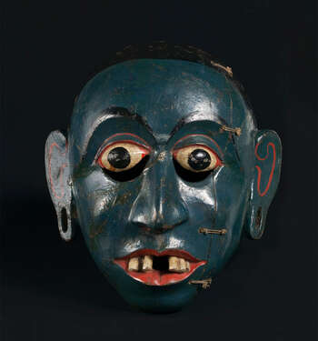 Ritual Function and Context: Kōlam theatre. UEM7037 represents an ancestor man or hunter from Sinhālese culture. The mask is known as Vaddā or Vadi Detū. The mask appears in Kōlam Theare with the masked character of the King Ancestor ( vaddi raju ). The mask is applied to narrate the story of Manāmē Kathawa or Chuĺlā Dhanūďdarā Jātakaya Katahawa. The key iconographic features of UEM7037 are: • Dark blue or green, black skin tone. • Red colour lips with missing tooth or uneven teeth ( dath boĺlēwa ) • Elongated ears with earring holes • A refine example of this character Tradition: Southern Dance Tradition/Low-Country Dance Tradition. This tradition is popular in Mātara, Bentōta, Ambalaňgoda in the Southern province and Olabodūwa in Rāiygama Kōralē in Western province of Sri Lanka. Materials and Techniques: Polychrome carved wood (White, red, green, black, blue).