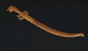 Ritual Function and Context: Kōlam theatre (?) UEM 7039 is a sword used by King characters. This object could be held by Mahāsammatha Mahasammataha Rajujuruwo or Manāmē Raju. This object is associated with royal characters who appeared in Kōlam Theatre. The key iconographic features of UEM7039 are: • The Lion Face (Siňhā-muhuna) in the arm grip • Fully intricate Sinhālese designs ( sinhālese môstharā ) • Colour palette from Sinhala Buddhist art in Temples. • This wooden sword is one of the refined examples of Sinhālese craft tradition. Tradition: Southern Dance Tradition/Low-Country Dance Tradition. This tradition is popular in Mātara, Bentōta, Ambalaňgoda in the Southern province and Olabodūwa in Rāiygama Kōralē in Western province of Sri Lanka. Materials and Techniques: Polychrome carved wood (white, yellow, red, black, blue).