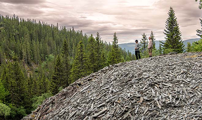 En mann står oppå en stor haug med steinbiter. Skog i bakgrunnen.