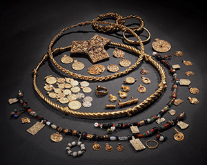 Golden jewellery and objects from the Viking Age displayed in a circle on a dark background.