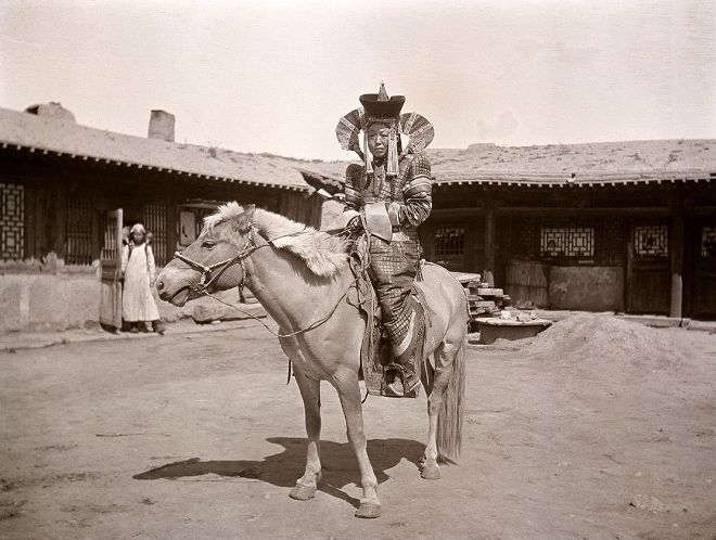 Mongolsk jente på hest, Ulan Bator 1912. Huset Oscar Mamen budde i, kan sjåast i bakgrunnen.