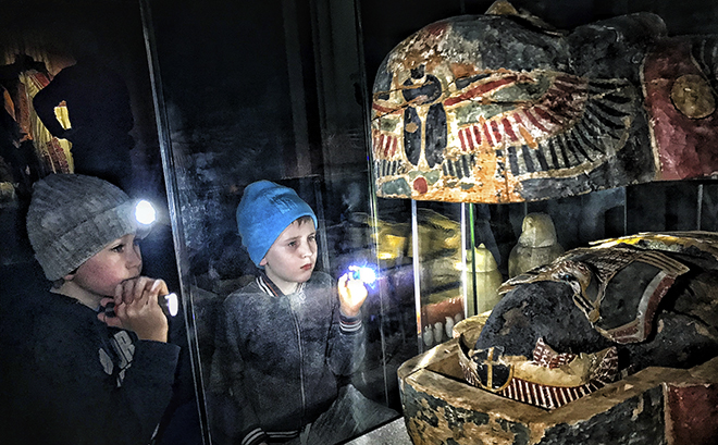 two children with flashlights looking at a mummy  