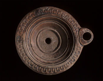 (C41906) Oljelampe av keramikk som måler 6,9 cm. i lengde og med en sirkulær form som er dekorert med konsentriske sirkler. Langs skulderen løper en bord av ovuler. Typen dateres til 70–100 e.Kr. Eksempelet kom til museet som en gjenstand i professor Arvid Andréns (1902–1999) samling.