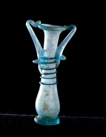 (C42172) Liten glassflaske på 11,4 cm. av typen unguentarium , som ble brukt til parfymerte oljer, og var svært utbredt i romersk tid, fra 100-tallet e.Kr. og fremover. Dette eksempelet har to hanker, og en spiral i blått glass dekorerer kroppen. Det er fra Midtøsten, og kom til museet som en gjenstand i Baron Platon von Ustinows (1840–1917) samling.