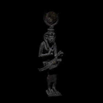 (C47109) Figur av bronse fra 664–305 f.Kr. med den egyptiske gudinnen Isis i ferd med å amme sønnen Horus. Den er 17 cm. høy, og var festet til en trone som har gått tapt. Gudinnen kjennes igjen på kronen, som består av to kuhorn og en solskive på et bånd av kobraer. Kjolen hennes er tettsittende, og hun byr sønnen sitt venstre bryst. Figuren er av en type som representerer Isis og Horus’ rolle som beskyttere, spesielt av barn. Figuren ble gitt i gave til museet før 1842, da den ble ført opp i aksesjonskatalogen.
