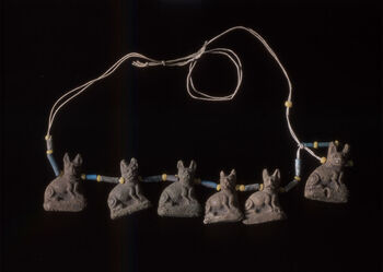 (C47551) Halsbånd bestående av perler med seks 2,5 cm. høye amuletter formet som sjakaler, eller mest sannsynlig, katter, som gjerne ble gjengitt med store ører i det gamle Egypt. Smykket dateres til ca. 1550–1295 f.Kr. Sjakalen representerte guden Anubis, som ifølge mytologien fulgte de døde til neste liv. Katten representerte gudinnen Bastet, hjemmets og familiens beskytter. Funnstedet er ukjent, og ble ikke angitt da smykket ble registrert ved museets samlinger omkring 1900.