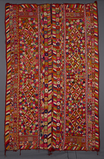 UEM49200. Teppet har triple border langs de fire kantene. De ytre loddrette bordene har det karakteristiske, flerfargede diagonale linjemønsteret. I hvert panel er det fire diamanter i et felt med blomster og andre motiver bestående av vegetabilske og levende skapninger som et skilpaddelignende dyr (med ører!), en sittende figur, insekter og også stjernelignende motiver.