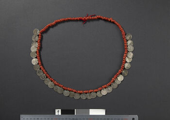(UEM46904) Glass eller keramiske perler og mynter tredd på bomullssnor. Dette er et mye brukt smykke som brukes til fest og ritualer. I 1993 da Kaban Rongpharpi, Dokmoka, lagde dette halskjedet, fantes ikke denne typen smykke ferdiglaget på markedet. Hun samlet mynter, gikk til smeden og fikk loddet på hempe, kjøpte perler og tredde det sammen på en bomullsnor.
