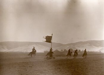(UEMf09893_014) Etter tilbedelsen av Bogd Khaan i Det gule palasset vendte Bogd hjem til Vinterpalasset, som kan sees i bakgrunnen på fotografiet. Soldater med bannere red foran Bogd.