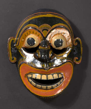 Rituell funksjon og kontekst: Sanniyäkuma/ Kōlam-teater UEM7032 kan være en demonkarakter. Masken kan representere en angstsykdom ( beētha sanniya ) eller kolera ( jala sanniya ). Karakteren brukes i Sanniyäkuma-ritualet. Demonkarakteren skaper en samtale av ord med doble betydninger og stygge ord ( kunuharupā ). UEM7032 har likheter med et apeansikt og kan som dyrekarakter også ha blitt brukt i Kōlam-teater. De viktigste ikonografiske trekkene ved UEM7032 er: • Mørkere hudtoner (svart, mørkeblå eller grønn) • Vidåpen munn med skarpe, korte tenner • Ansiktsuttrykk for frykt • Åpen munn som gjør det lettere for danseren å snakke • Mindre i størrelse • Deformasjon av menneskelige trekk • Fremstilling av begrensede singalesiske motiver ( môstharā ). Tradisjon: Sanniyäkuma eller Dahata Sanniya Shānthi-Kařmayã. Dette helbredelsesritualet antas å stamme fra Bali-ritualet og er populært i Mātara, Gāll, Bentōta i den Sørprovinsen og i Olabodūwa, Rāiygama Kōralē, i Vestprovinsen på Sri Lanka. Det er betydelige forskjeller mellom hvordan dette ritualet holdes i Mātara og Bentōta. Materialer og teknikker: Polykromt utskåret treverk, (hvit, gul, rød og svart).